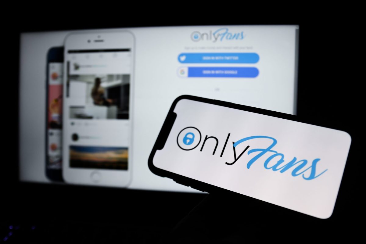Bilgisayar ekranında OnlyFans'ın ana sayfası, önündeki telefonda OnlyFans'ın logosu görünüyor.