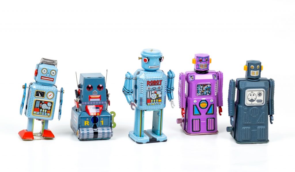 Beş farklı oyuncak robot beyaz arka plan önünde duruyor. Dördüncüsü mor renkte, diğerleri mavinin farklı tonlarında.