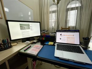 200. bülteni yazdığım çalışma masasının fotoğrafı. Sol tarafta ikinci mönitör, kalemler ve başka ekstralar var. Ön ve sağ taraftaki masada macbook bilgisayar, bir not defteri ve üstünde dolmakalem, yanında How to Future isimli bir kitap, onların arkasına doğru da Kindle, Raspberry Pi gibi ekstra eşyalar duruyor.
