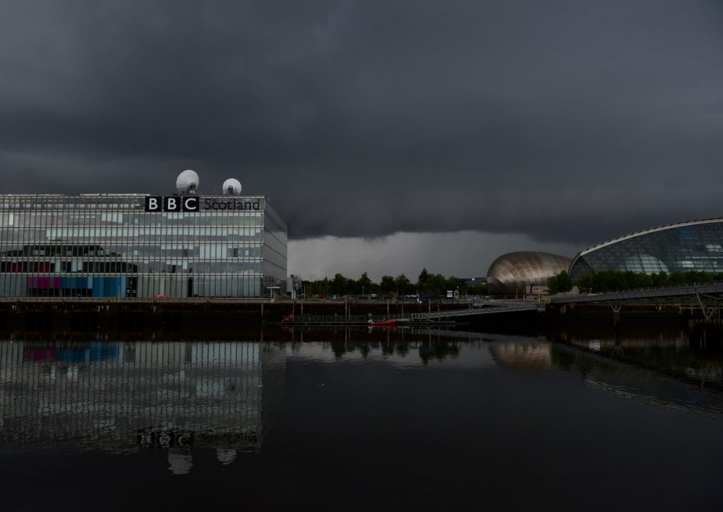 BBC Scotland binasının uzaktan, önündeki nehri de alacak şekilde çekilmiş bir fotoğrafı. Arka planda gökyüzündeki kara bulutlar görünüyor ve karamsar bir hava yaratıyor.