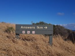 Dağlık bir alandaki yol tabelasının üzerinde Answers (Cevaplar) 1 kilometre sağda yazıyor.