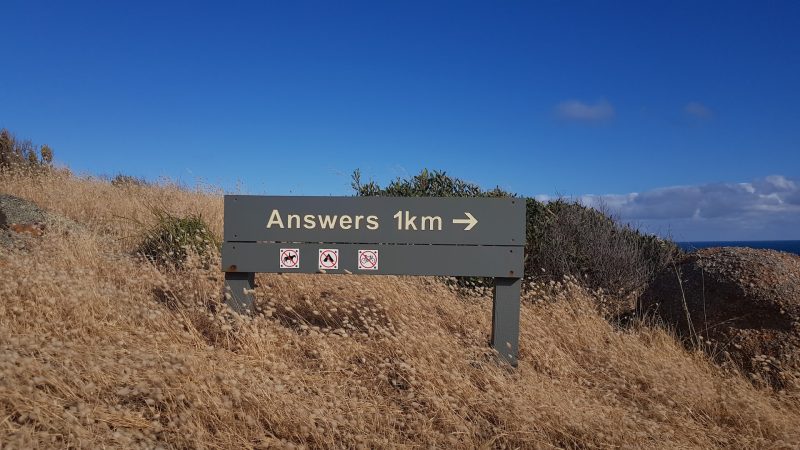 Dağlık bir alandaki yol tabelasının üzerinde Answers (Cevaplar) 1 kilometre sağda yazıyor.