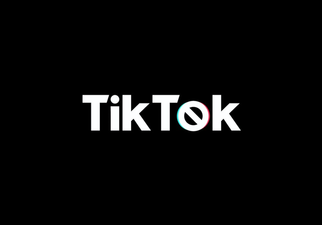 Siyah üzerine beyaz yazıyla TikTok yazıyor, ancak o harfi yasaklama sembolü gibi ve etrafında TikTok logosuna benzer renkli dalgalar var. 