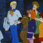 Scooby Doo ekibi bağlayıp maskesini çıkardıkları bir kötü karakterin başında duruyor ve yanlarındaki polise bir şeyler anlatıyor.