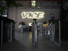 Vice ofislerinin girişinden çekilmiş bir fotoğraf. Güvenlik kapılarının arkasındaki beyaz duvarda LED ışıklarla yazılmış Vice logosu görülüyor.