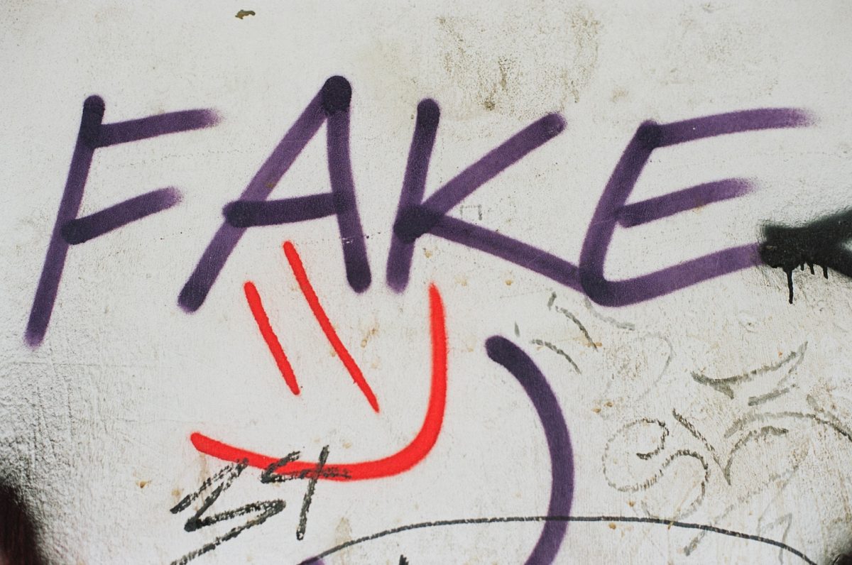 Bir duvardaki graffitide mor renkte fake yazılmış. Altında da kırmızı renkle gülen bir yüz çizilmiş.