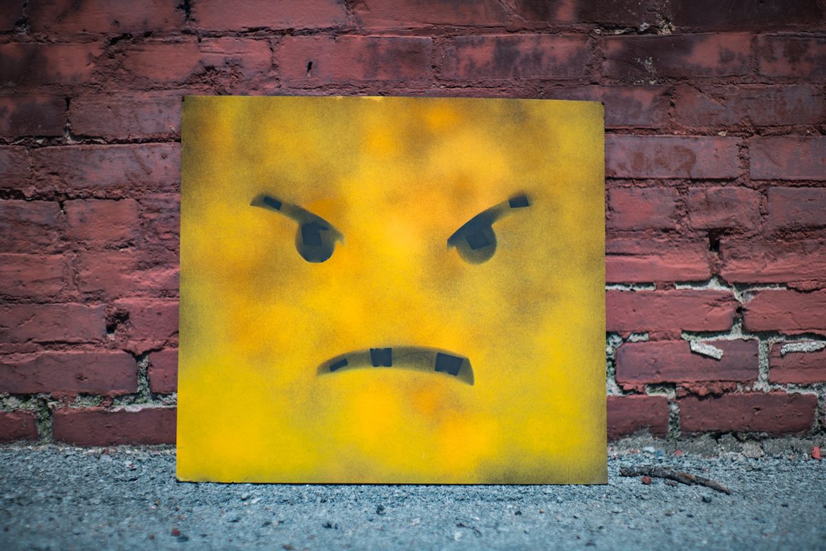 Bir duvarın önünde kare bir plakanın üzerine kızgın bir emoji yüzü çizilmiş.