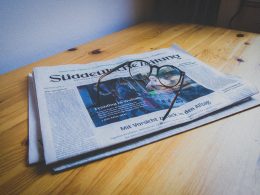 Ahşap bir masanın üzerinde Süddeutsche Zeitung gazetesi ve onun üzerinde de bir gözlük duruyor.