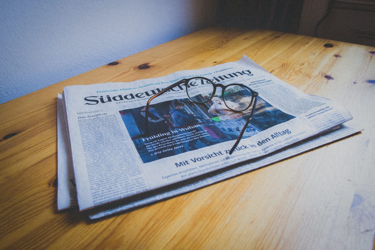 Ahşap bir masanın üzerinde Süddeutsche Zeitung gazetesi ve onun üzerinde de bir gözlük duruyor.