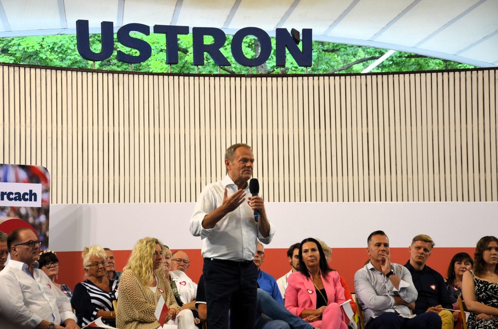 Polonya başbakanı Donald Tusk'ın seçim dönemi açık oturumlardan birisinde çekilmiş fotoğrafı. Ayakta duran Tusk elinde bir mikrofonla konuşuyor, etrafında sandalyelere oturmuş onu dinleyen insanlar var.