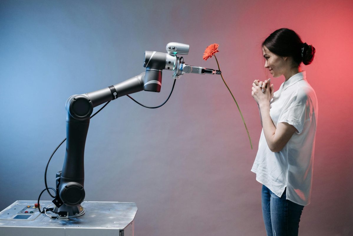 Robot bir kol, beyaz gömlek ve kot pantolon giymiş bir kadına çiçek uzatıyor.