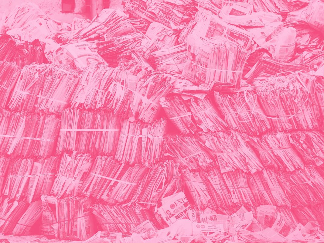 Eski gazetelerden oluşan bir yığının fotoğrafına koyu pembe bir filtre uygulanmış.