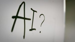 Beyaz bir yazı tahtasının üstünde siyahla "AI?" yazıyor.