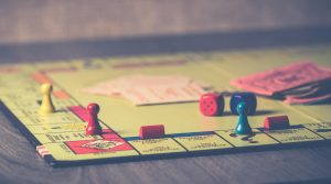 Bir masanın üzerinde yarıda bırakılmış bir Monopoly oyunu var. Üç oyuncu taşı, iki zar, oyun kartları ve parası oyun tahtasının üzerinde duruyor.