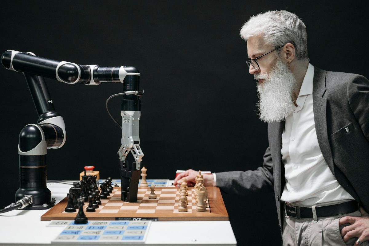 Bir robotla beyaz sakallı bir adam masanın başında karşılıklı satranç oynuyor.